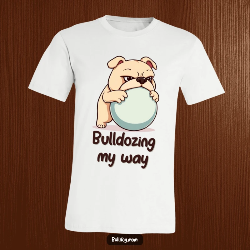 Funny T-shirt featuring a bulldog with a determined gaze, actively pushing a large ball, symbolizing strength and perseverance.